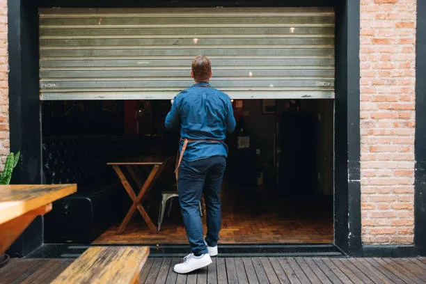 A business owner rolling up the shutter to open a coffee shop